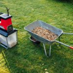 Gartenhäcksler und Schubkarre mit gehäckseltem Material auf einer Wiese